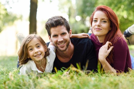 Happy young family in a urban park. Father, mother and little daughter laying on grass.