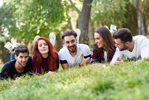 Group of young people together outdoors in urban park. Women and men laying on grass wearing casual clothes.