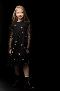 Cute little girl in a beautiful dress on a black background. Studio photo.