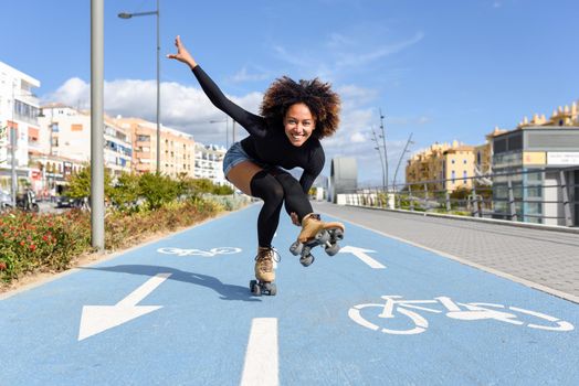 Young fit black woman on roller skates riding outdoors on bike line. Smiling girl with afro hairstyle rollerblading on sunny day