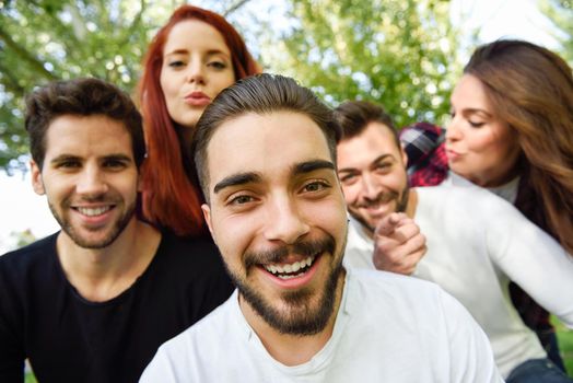 Group of friends taking selfie in urban background. Five young people wearing casual clothes.