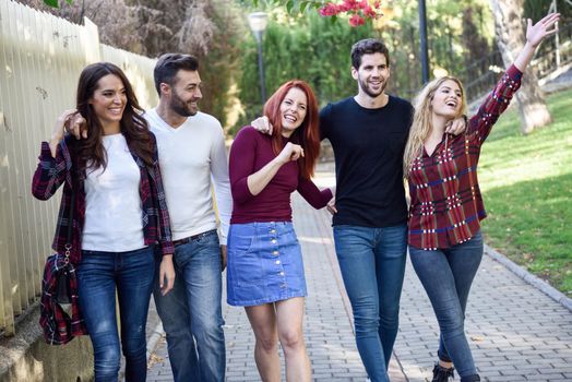 Group of young people together outdoors in urban background. Women and men sitting on stairs in the street wearing casual clothes.