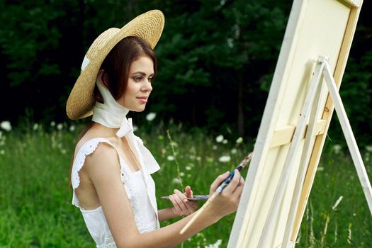 pretty woman in hat artist paints a picture on nature paint. High quality photo