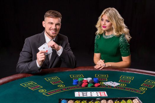 couple playing poker at the green table. The blonde girl and a guy in a suit. happy win, two aces