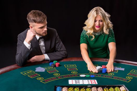 couple playing poker at the green table. The blonde girl and a guy in a suit. all-in bets chips