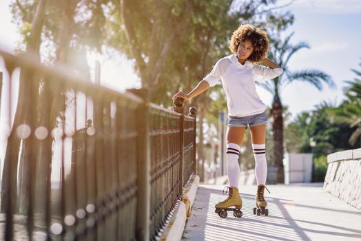 Young black woman on roller skates riding near the beach. Girl with afro hairstyle rollerblading on sunny promenade with sun backlight.