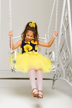 Beautiful little girl swinging in the studio on a swing. Concept of a happy childhood, family well-being.