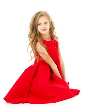 Portrait of a cute preteen girl sitting on the floor with her knees, adorable girl with long blond hair wearing a red fashionable dress posing, in the studio on a white background