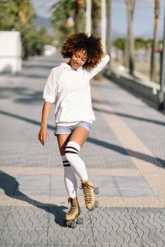 Smiling black woman on roller skates riding outdoors on beach promenade with palm trees. Smiling girl with afro hairstyle rollerblading on sunny day.