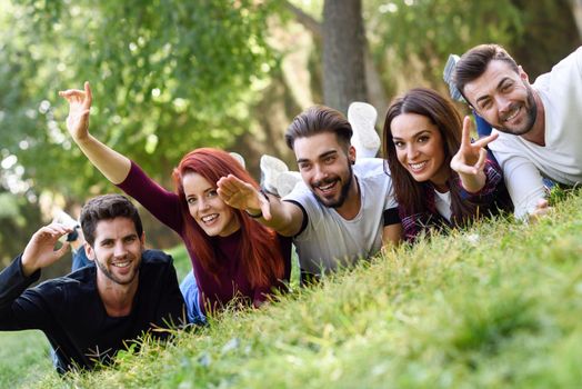 Group of young people together outdoors in urban park. Women and men laying on grass wearing casual clothes.