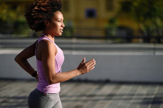 Black woman, afro hairstyle, running outdoors in urban road. Young female exercising in sport clothes.