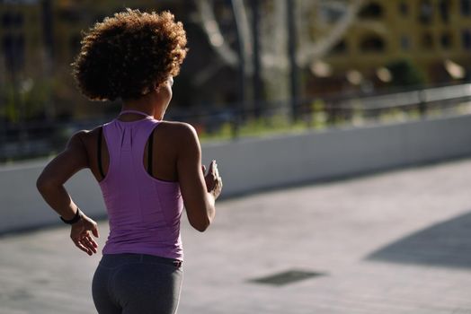 Rear view og black woman, afro hairstyle, running outdoors in urban road. Young female exercising in sport clothes at Sunset.