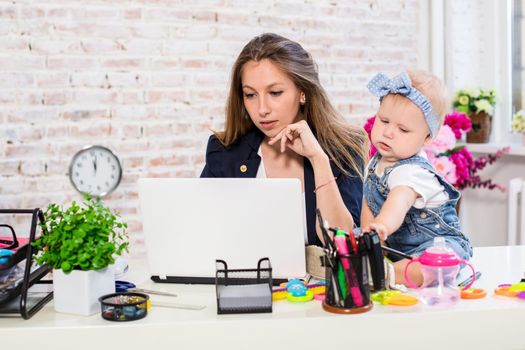 Working together is so fun Cheerful young beautiful businesswoman looking at laptop while sitting at her working place with her little daughter