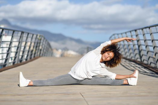 Young black woman doing stretching after running outdoors. Girl exercising with city scape at the background. Afro hair.