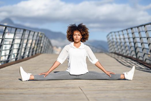 Young black woman doing stretching after running outdoors. Girl exercising with city scape at the background. Afro hair.