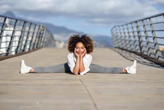 Young black woman doing stretching after running outdoors. Girl exercising with city scape at the background. Afro hair.