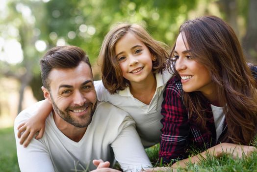 Happy young family in a urban park. Father, mother and little daughter laying on grass.