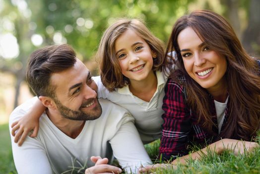 Happy young family in a urban park. Father, mother and little daughter laying on grass.