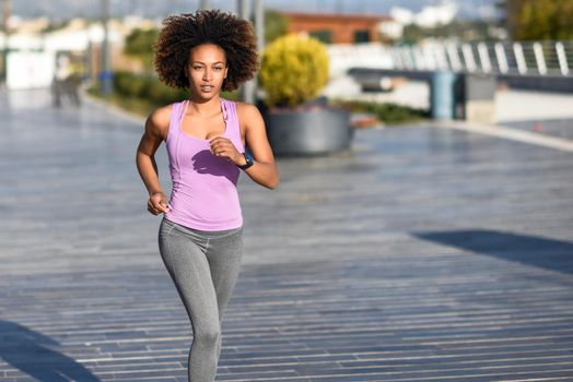 Black woman, afro hairstyle, running outdoors in urban road. Young female exercising in sport clothes.