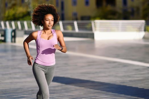 Black woman, afro hairstyle, running outdoors in urban road. Young female exercising in sport clothes.
