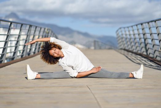 Young black woman doing stretching after running outdoors. Girl exercising with city scape at the background. Afro hair.