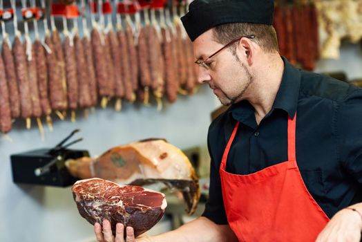 Butcher with a piece of ham in his hand inside a butcher shop