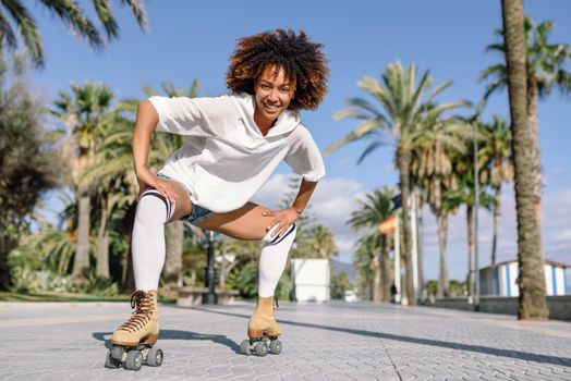 Smiling black woman on roller skates riding outdoors on beach promenade with palm trees. Smiling girl with afro hairstyle rollerblading on sunny day.