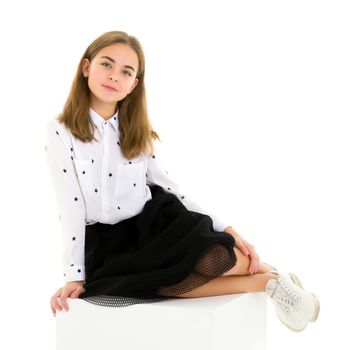 Front View Portrait of Beautiful Blonde Girl in Elegant Dress Sitting on Cube in Studio, Cheerful Long Haired Girl Wearing Fashionable Stylish Clothes Posing Against White Background