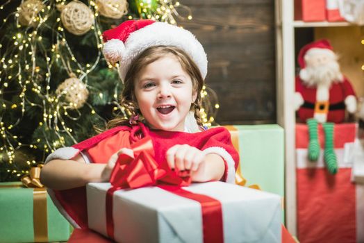 Excited cute child opening a Christmas present. Christmas kid girl holding a red gift box