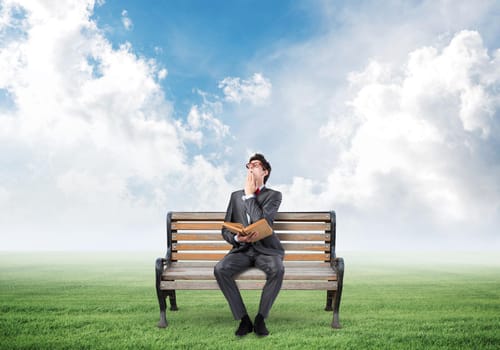 a young student sits on a wooden bench and holds a book. looks up