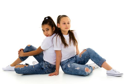 Two cute little girls are sitting on the floor in a studio on a white background. Concepts of style and fashion, happy childhood. Isolated.