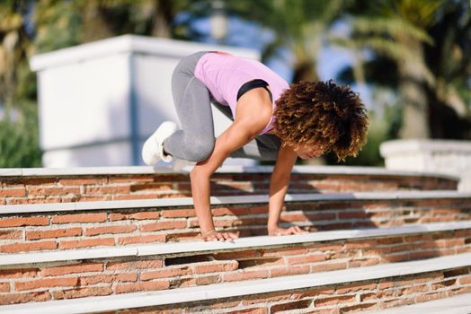 Black fit woman doing fitness acrobatics in urban background. Young female exercising and working out hard.