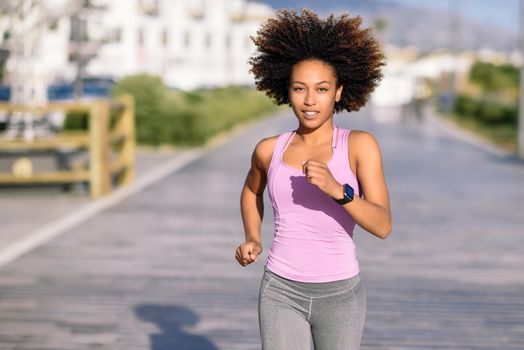 Black woman, afro hairstyle, running outdoors in urban road. Young female exercising in sport clothes.