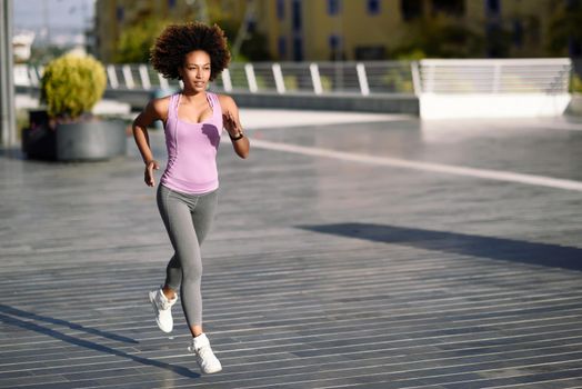 Black woman, afro hairstyle, running outdoors in urban road. Young female exercising in sport clothes.