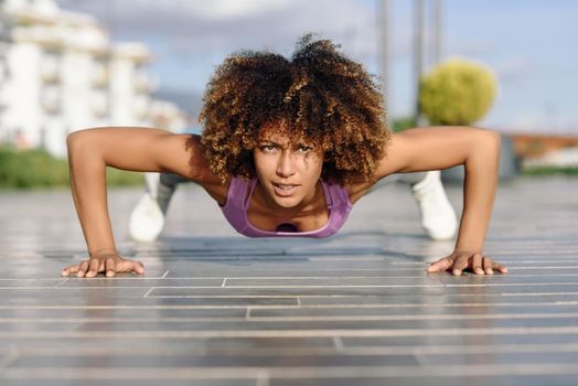 Black fit woman doing pushups on urban floor. Young female working out in the street.