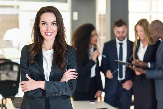 Businesswoman leader looking at camera in modern office with multi-ethnic businesspeople working at the background. Teamwork concept. Caucasian woman.