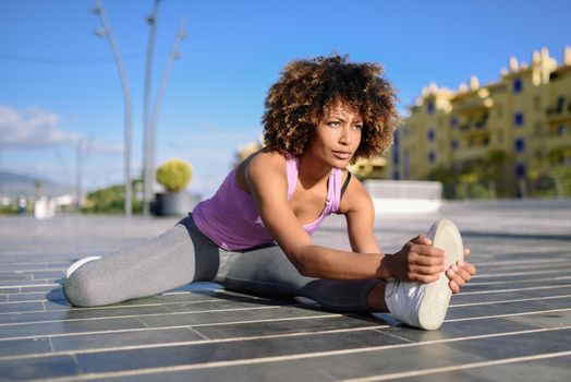 Young black woman doing stretching after running outdoors. Girl exercising with city scape at the background. Afro hair.