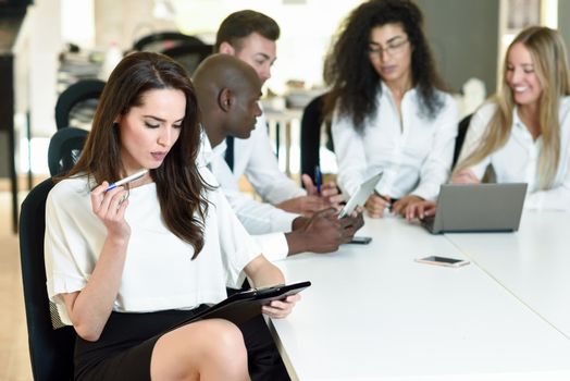 Multi-ethnic group of five businesspeople meeting in a modern office. Caucasian businesswoman leader, wearing white shirt and black skirt, looking at camera.