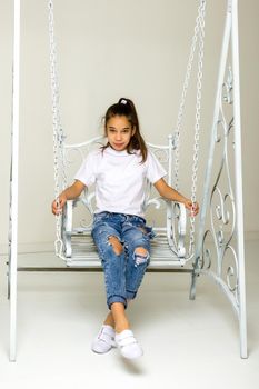 Beautiful little girl swinging in the studio on a swing. Concept of a happy childhood, family well-being.