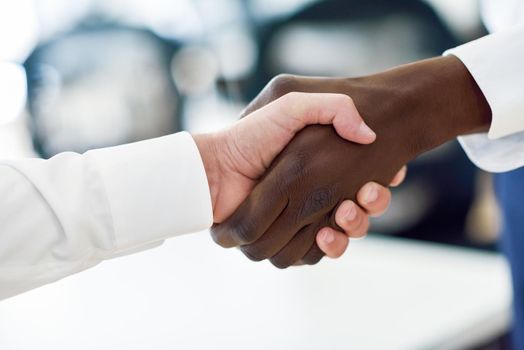 Black businessman shaking hands with a caucasian one wearing suit in an office. Close-up shot