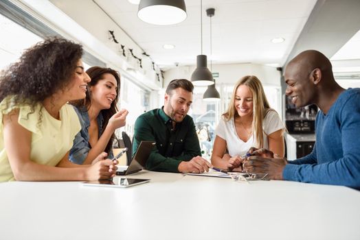 Five young people studying with laptop and tablet computers on white desk. Beautiful girls and guys working toghether wearing casual clothes. Multi-ethnic group smiling.