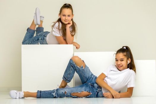 Two little girls posing in the studio on white cubes. The concept of tenderness and beauty.