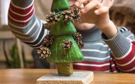 A little boy decorates a hand-made Christmas tree with pine cones and at the same time plays funny