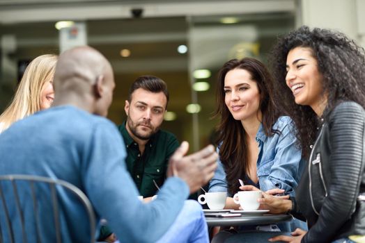 Multiracial group of five friends having a coffee together. Three women and two men at cafe, talking, laughing and enjoying their time. Lifestyle and friendship concepts with real people models