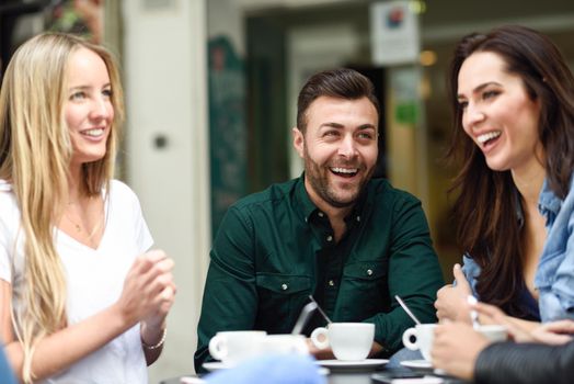 Multiracial group of friends having a coffee together. Two women and a man at cafe, talking, laughing and enjoying their time. Lifestyle and friendship concepts with real people models