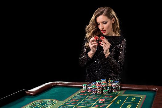 Sexy woman in a black dress playing in casino. Woman stakes piles of chips playing roulette at the casino club. Gambling. Roulette.