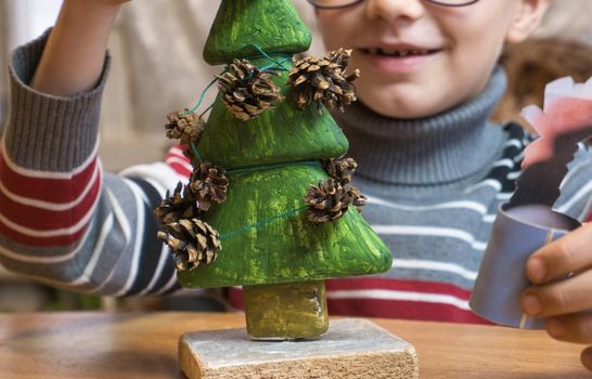 A little boy decorates a hand-made Christmas tree with pine cones and at the same time plays funny