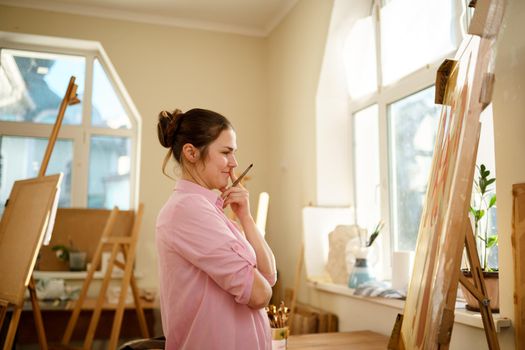 Female artist working in studio. Creative workspace, painting class, easel with canvas, art therapy. Inspiration, creativity, talent, craft concept. Artist studio interior. People, leisure and hobby.