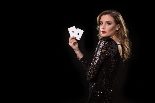 Young beautiful woman in black shiny dress holds poker cards in hands against a black background. The concept of gambling. Casino