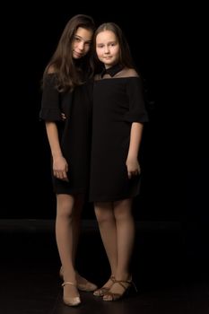 Two cute little girls posing in the studio on a black background. Style and fashion concept, layout for magazine cover.